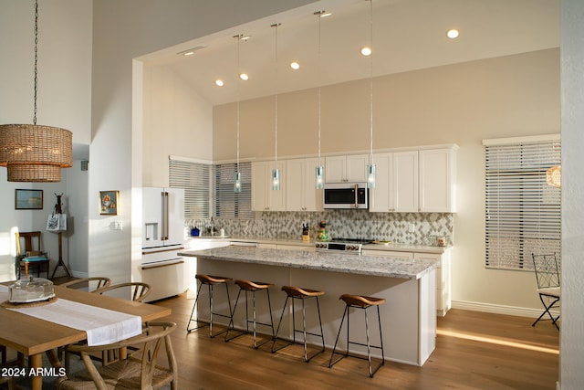 kitchen with high quality appliances, high vaulted ceiling, white cabinets, hardwood / wood-style flooring, and light stone counters