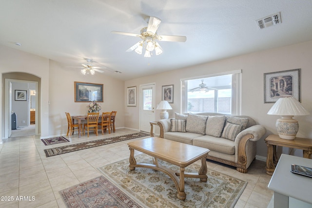 living room featuring a ceiling fan, visible vents, baseboards, arched walkways, and light tile patterned flooring