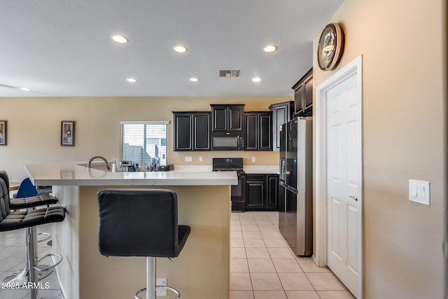 kitchen featuring a center island with sink, black appliances, a kitchen bar, and light tile patterned floors