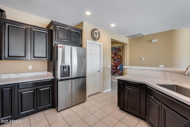 kitchen featuring light tile patterned flooring, sink, light stone countertops, and stainless steel refrigerator with ice dispenser