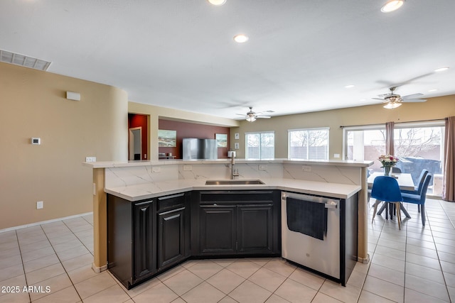 kitchen featuring a kitchen island with sink, sink, dishwasher, light tile patterned floors, and decorative backsplash