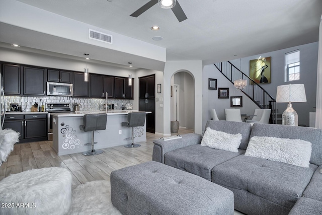 living room featuring light wood finished floors, visible vents, arched walkways, ceiling fan, and stairs