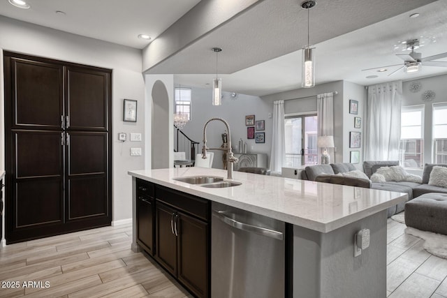 kitchen with a sink, open floor plan, stainless steel dishwasher, an island with sink, and decorative light fixtures