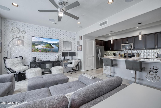 living room with wallpapered walls, visible vents, a ceiling fan, light wood-style flooring, and recessed lighting