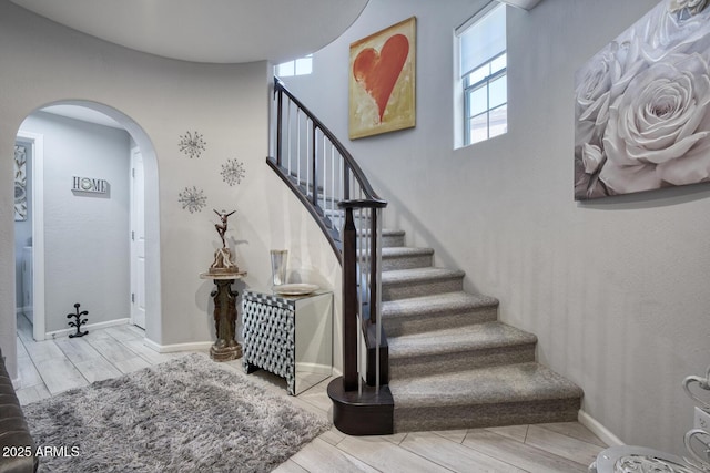 staircase with baseboards, arched walkways, and wood finish floors