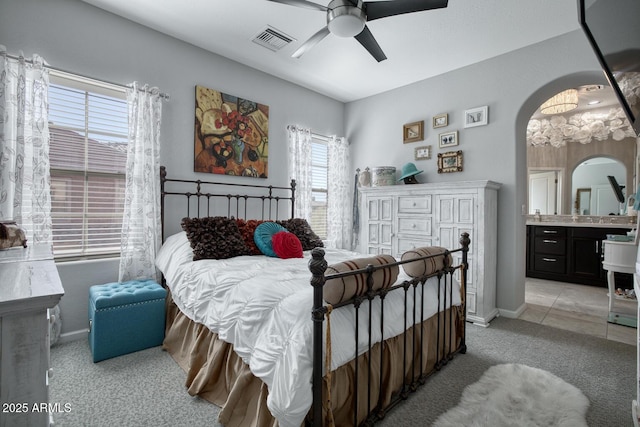 bedroom with light carpet, visible vents, arched walkways, ceiling fan, and ensuite bath