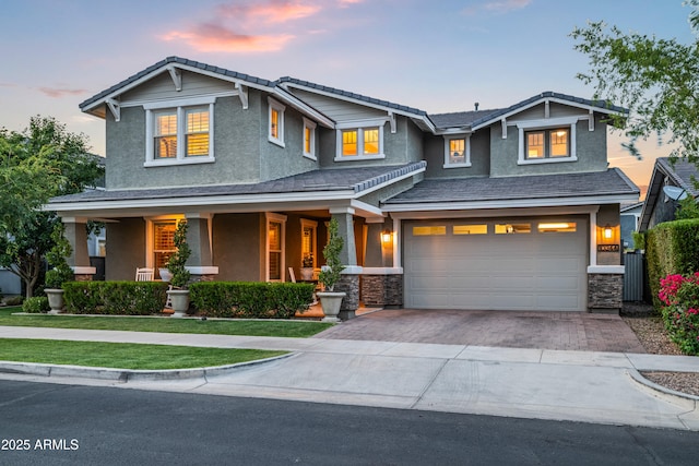 craftsman inspired home featuring an attached garage, a porch, decorative driveway, stone siding, and stucco siding