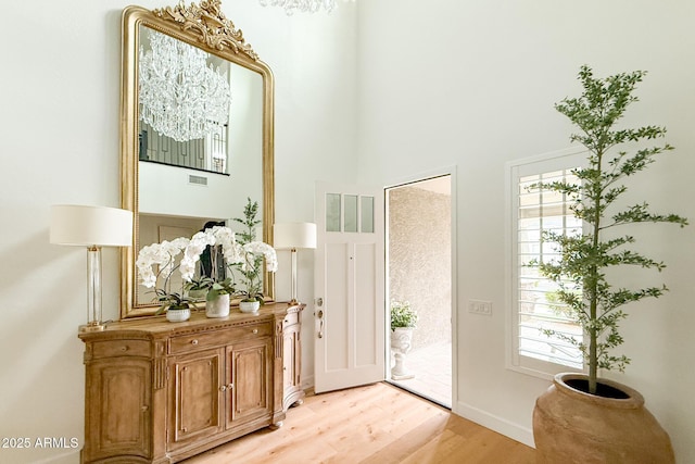 entryway with light wood-type flooring, healthy amount of natural light, a high ceiling, and baseboards