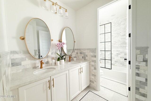 bathroom with tile walls, toilet, double vanity, tile patterned flooring, and a wainscoted wall