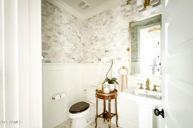 bathroom featuring toilet, a wainscoted wall, and ornamental molding