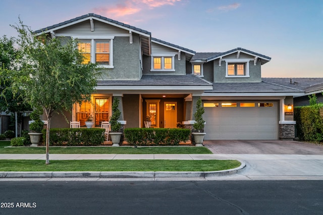 craftsman-style house featuring driveway, stucco siding, an attached garage, a porch, and a front lawn