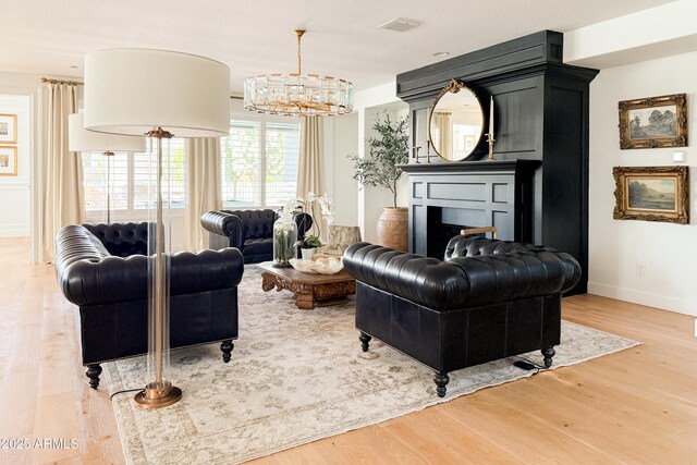 living room featuring light wood-type flooring, a chandelier, baseboards, and a fireplace