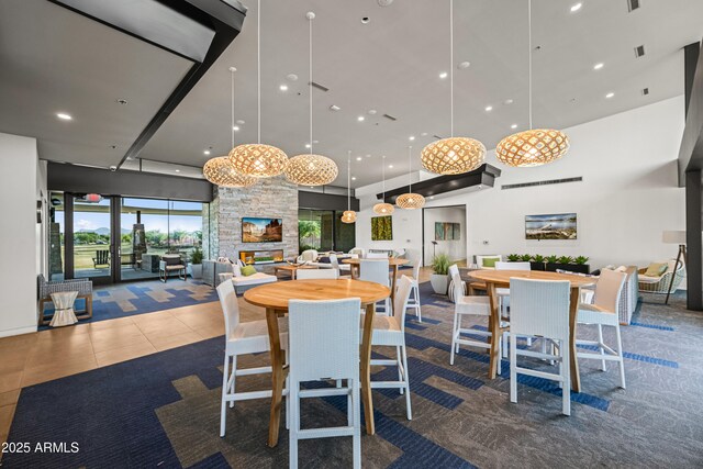 dining room featuring a towering ceiling, a stone fireplace, and recessed lighting