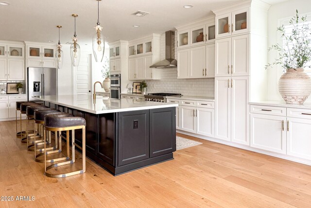kitchen featuring appliances with stainless steel finishes, wall chimney exhaust hood, decorative backsplash, light wood-type flooring, and recessed lighting