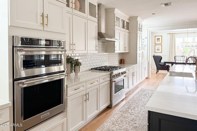 kitchen featuring stainless steel appliances, wall chimney exhaust hood, a sink, light wood-style flooring, and recessed lighting