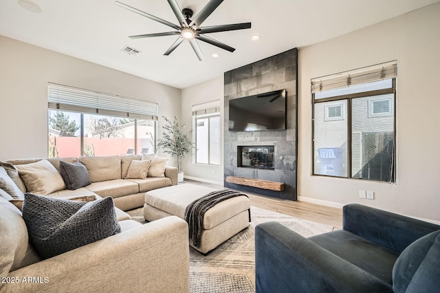 living room featuring light wood finished floors, baseboards, visible vents, and a tile fireplace