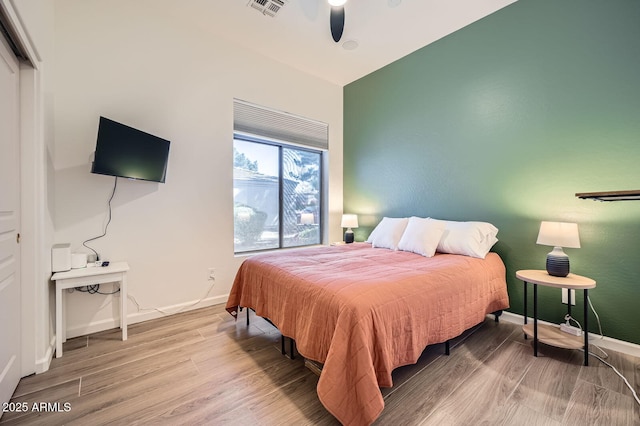 bedroom with a ceiling fan, visible vents, baseboards, and wood finished floors