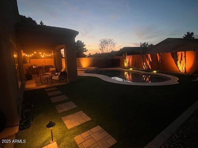 pool at dusk with a patio, a fenced backyard, and an outdoor pool