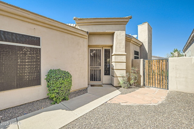 property entrance featuring a chimney, a gate, and stucco siding