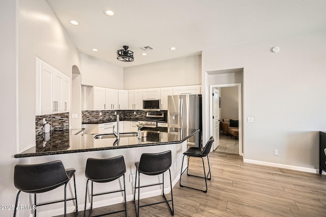 kitchen with a peninsula, a sink, visible vents, appliances with stainless steel finishes, and decorative backsplash