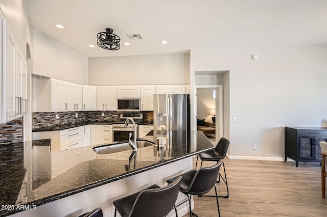 kitchen featuring stainless steel appliances, visible vents, light wood-style flooring, decorative backsplash, and a sink