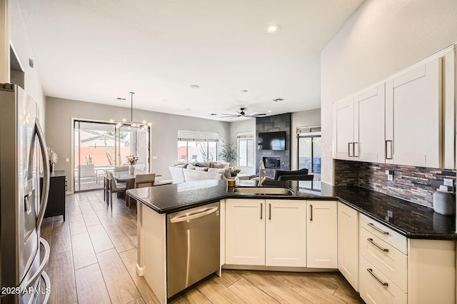 kitchen featuring appliances with stainless steel finishes, open floor plan, a peninsula, backsplash, and ceiling fan with notable chandelier