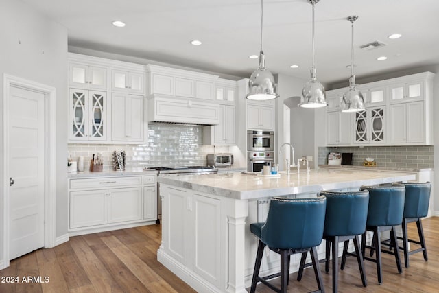 kitchen with a large island, decorative backsplash, white cabinets, hanging light fixtures, and light wood-type flooring