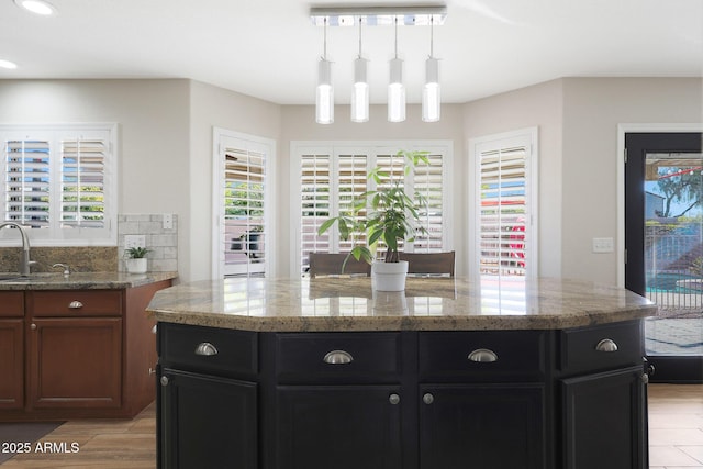 kitchen featuring decorative light fixtures, light stone countertops, sink, and a kitchen island