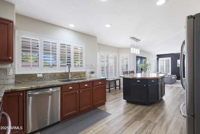 kitchen featuring a kitchen island, pendant lighting, sink, stainless steel appliances, and light stone countertops