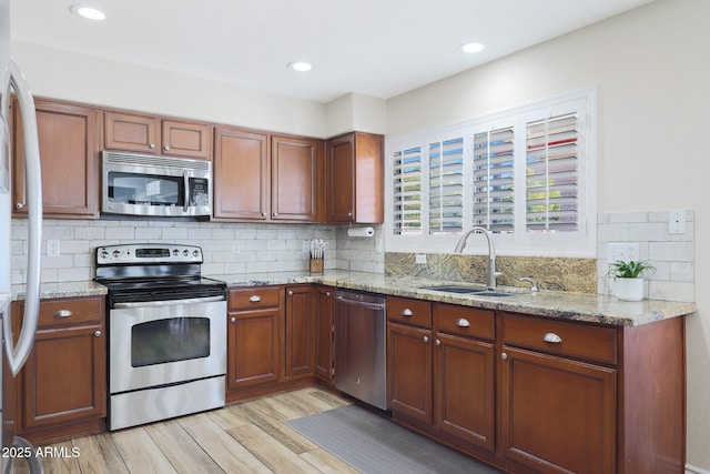 kitchen featuring sink, light stone counters, appliances with stainless steel finishes, light hardwood / wood-style floors, and backsplash