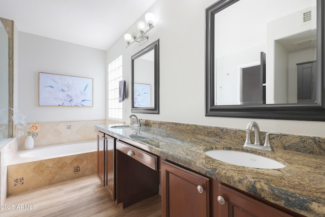 bathroom with hardwood / wood-style floors, vanity, and a relaxing tiled tub