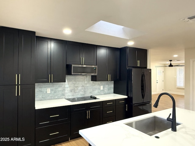 kitchen featuring sink, tasteful backsplash, light stone counters, light hardwood / wood-style flooring, and black appliances