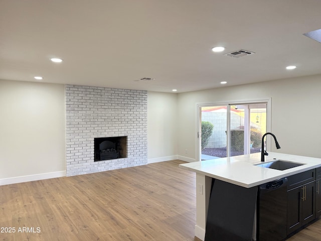 kitchen featuring black dishwasher, sink, a fireplace, and light wood-type flooring