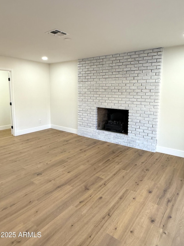 unfurnished living room featuring a brick fireplace and light wood-type flooring