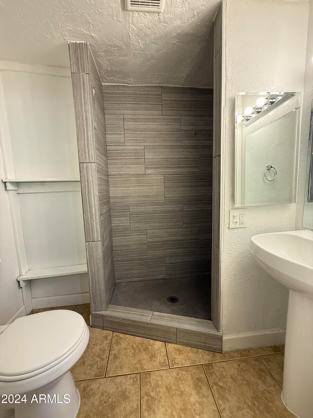 bathroom featuring tile patterned floors, a textured ceiling, a tile shower, and toilet