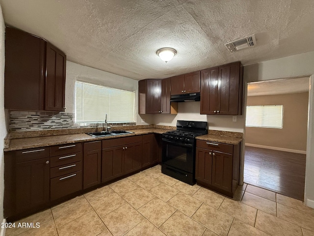 kitchen featuring gas stove, dark brown cabinetry, sink, a textured ceiling, and light tile patterned flooring