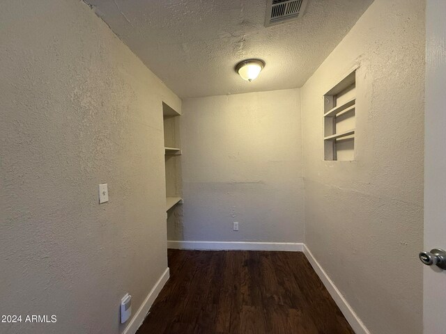 hallway featuring built in shelves, a textured ceiling, and dark hardwood / wood-style floors