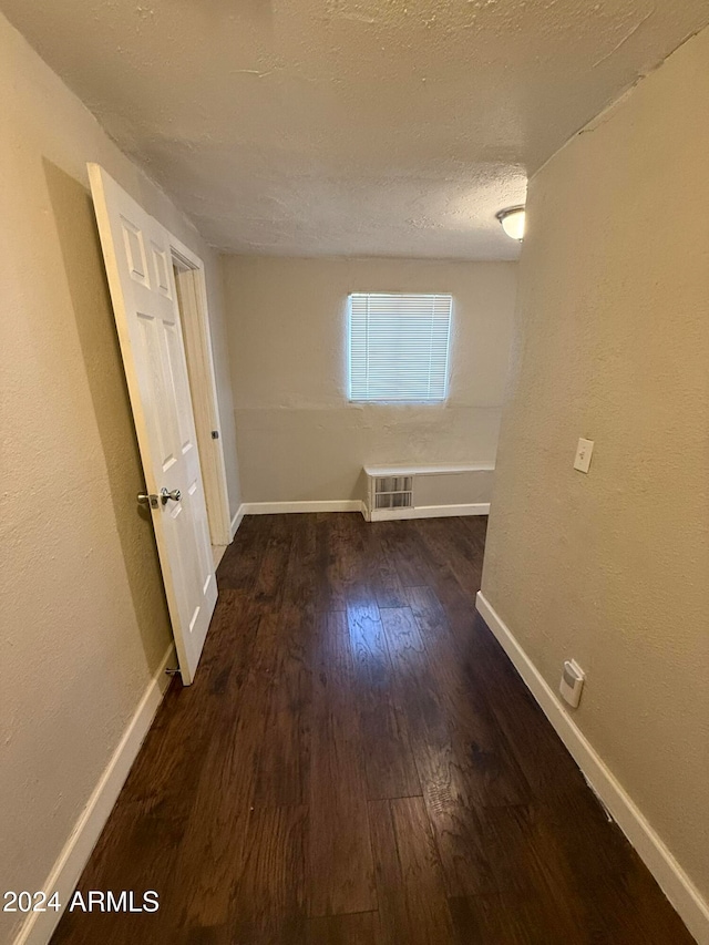 corridor with a textured ceiling and dark wood-type flooring