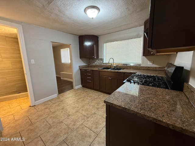 kitchen with stove, backsplash, sink, a textured ceiling, and dark brown cabinetry