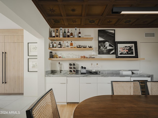 bar with coffered ceiling, white cabinetry, and light stone countertops