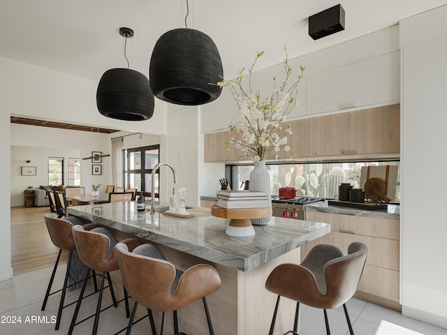 kitchen featuring a kitchen island with sink, light tile patterned floors, and decorative light fixtures