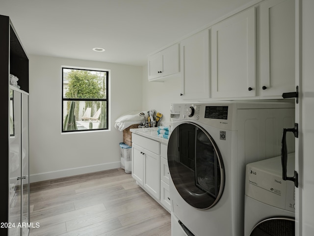 laundry area featuring washer and clothes dryer, light hardwood / wood-style floors, and cabinets