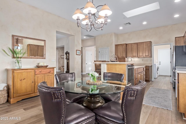 dining room featuring a notable chandelier, washer / dryer, a skylight, and light wood-type flooring