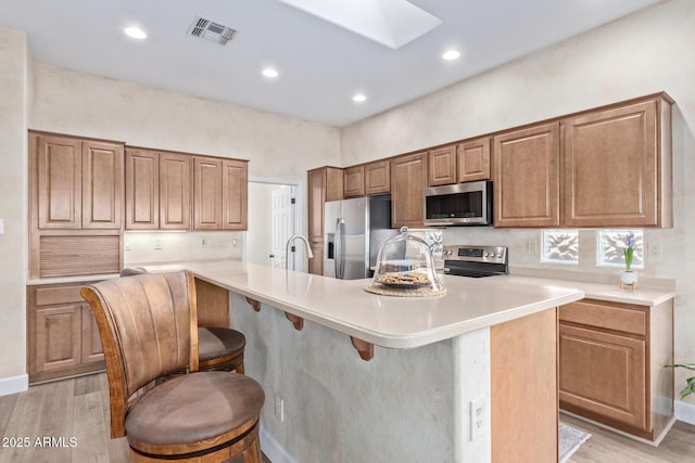 kitchen with light hardwood / wood-style flooring, a breakfast bar, a skylight, stainless steel appliances, and a center island with sink