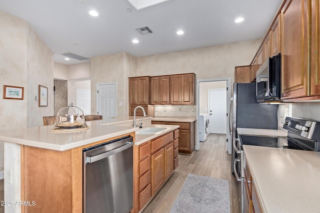 kitchen with washer / dryer, sink, light hardwood / wood-style flooring, an island with sink, and stainless steel appliances