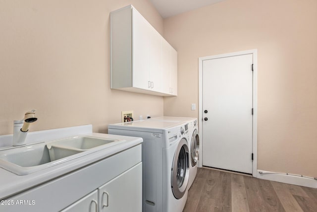 laundry area with cabinets, sink, washer and clothes dryer, and light hardwood / wood-style flooring