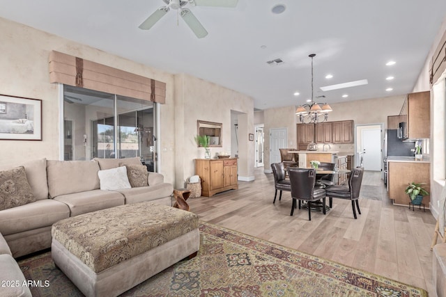 living room with ceiling fan with notable chandelier and light wood-type flooring