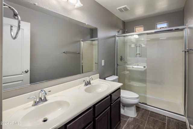 bathroom featuring toilet, a shower stall, double vanity, wood tiled floors, and a textured wall