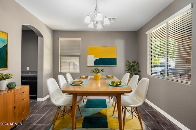 dining space featuring visible vents, wood finish floors, baseboards, arched walkways, and a notable chandelier