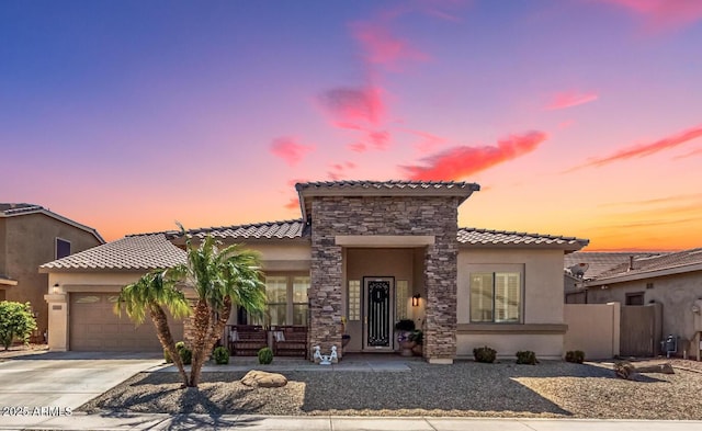 mediterranean / spanish-style home featuring fence, an attached garage, stucco siding, concrete driveway, and stone siding